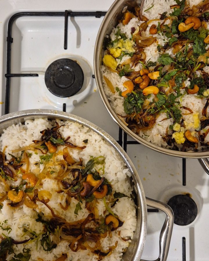 Two pans of homemade biryani topped with fried onions, cashews and coriander
